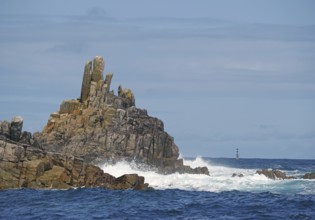 Barren rock formations by the sea with waves, a lighthouse visible in the distance, St Agnes, Isles