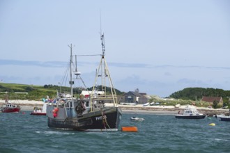 Fishing boat on the sea near the coast, surrounded by smaller boats, Hugh town, Isles of Scilly,