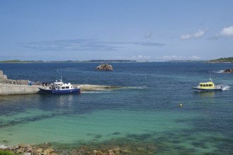 Two boats in the harbour area with a view of the open sea and distant islands under a blue sky, St
