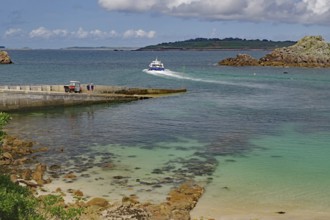 A boat approaches the harbour on clear blue water surrounded by rocks and islands, Ferry, St Agnes,