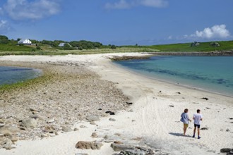 Two people walking along a soft sandy beach with blue sea and sky, St Agnes, Isles of Scilly,