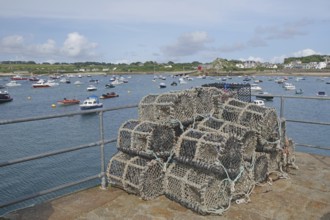 A harbour with stacked lobster pots, many boats on the water and a coastline in the background,