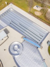 Aerial view of an empty swimming pool with a small playground nearby, renovation of the swimming