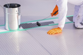 A person applies paint to the floor with a paint roller, next to it a bucket, renewal of the