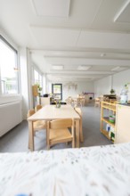 Bright kindergarten room with wooden furniture and large windows, transitional containerised