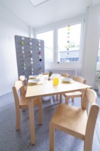 Modern dining area with wooden furniture and colourful window decorations, transitional daycare