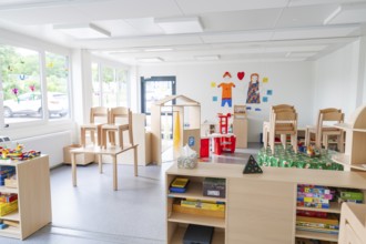 Bright room with toys, set-up chairs and shelves in the foreground, transitional daycare centre in
