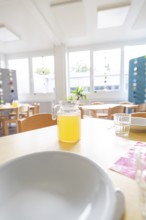 Close-up of a laid table with juice jug and bright window light, transitional daycare centre in