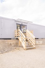 Modern entrance to a grey modular building with wooden stairs, transitional daycare centre in