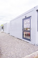 Grey containers with doors in a functional outdoor area, transitional daycare centre in container