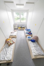 Overview of a dormitory for children with beds, lit by windows, transitional containerised daycare