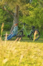 A person sits on a bench under a tree next to a bicycle in nature, e-bike excursion, Gechingen,