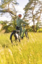 A person stands with a bicycle in the grass, surrounded by sunlight, e-bike excursion, Gechingen,