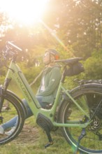 Person with helmet sitting next to a bicycle, enjoying nature in the warm sunlight, e-bike