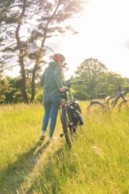 A person pushes a bicycle through high grass in a sunny field, e-bike excursion, Gechingen,