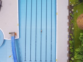 A swimmer swimming laps in a large swimming pool surrounded by green areas, Calw outdoor pool,