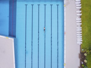 Drone shot of an empty swimming pool with a swimmer in a turquoise-coloured pool on a summer's day,