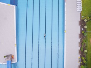 A swimmer moves in a large, empty pool next to a green meadow, Calw outdoor pool, Black Forest,