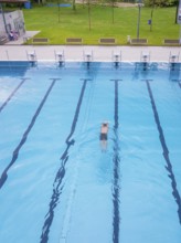 A swimmer swims in an empty, large swimming pool in sunny weather, Calw outdoor pool, Black Forest,