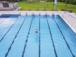 A swimmer swims in the large, clear pool on a sunny day, Calw outdoor pool, Black Forest, Germany