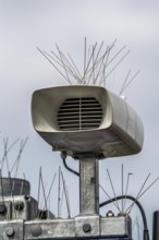 Loudspeakers on a scoreboard, at a railway station, studded with thin wires against birds, pigeons,
