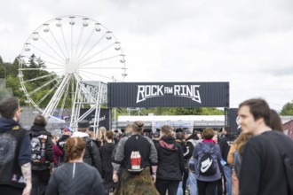 Festival visitors in front of a Ferris wheel and a container with the Rock am Ring logo at the Rock