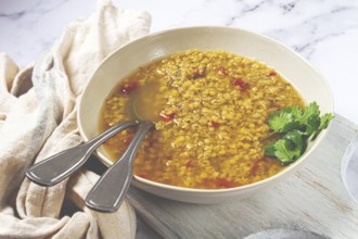 A hearty lentil soup is beautifully presented in a beige bowl, garnished with fresh herbs, placed