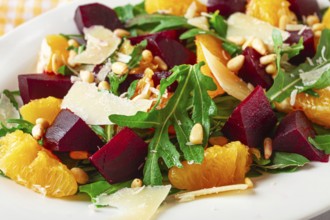 A salad made with chunks of beet, orange slices, and arugula. It is topped with cheese shavings and