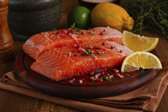 Two salmon fillets rest on a wooden platter. The fillets are garnished with herbs and spices. Lemon