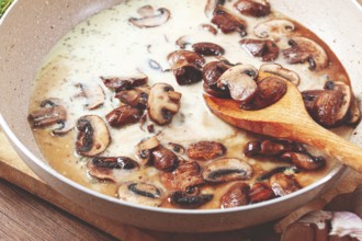 Mushrooms are cooking in a creamy sauce with garlic and herbs in a pan. Fresh thyme and garlic are