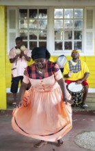 Guatemalan woman in traditional dress singing and dancing, men playing music in the back, Garifuna