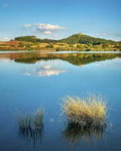 Wachsenburg Castle is reflected in the still water of a lake under a blue sky with cumulus clouds,