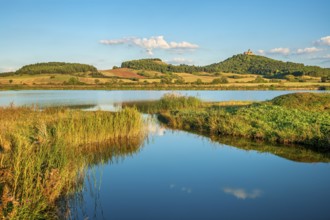 Wachsenburg Castle is reflected in the still water of a lake under a blue sky with cumulus clouds,