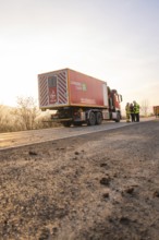 A fire truck is parked on a street at sunrise with firefighters nearby, fire department practice at