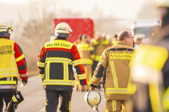 Firemen in yellow and red uniforms walk on a country road, accompanied by colleagues, fire brigade
