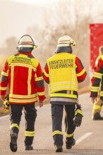 Firefighters walk together on a street, operational clothing and equipment visible, fire brigade