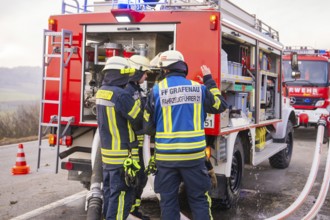 Firemen in emergency clothing stand at an emergency vehicle and check hoses, fire brigade exercise