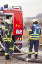 Firemen deployed next to a red fire truck. They wear helmets and special uniforms, fire department