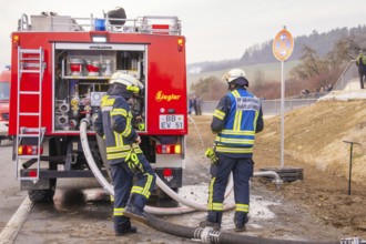Firefighters are standing on a street near a fire truck. They are preparing hoses for use, fire