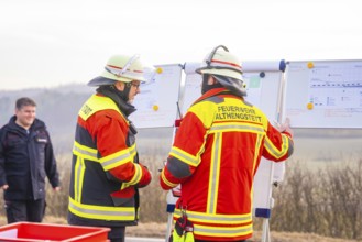 Firefighters in operational clothing during mission briefing in front of a rural backdrop, fire