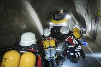 In the tunnel, a train of firefighters is sprayed with water. Respiratory equipment is worn, fire