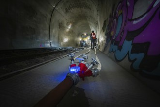 A fire hose in the foreground of a tunnel sprayed with graffiti, fire department exercise on the