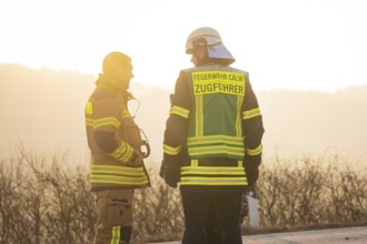 Two firefighters talking at sunset wearing safety vests on a street, fire department exercise on