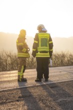 Two firefighters in protective clothing stand on a street at sunset, fire brigade exercise on the