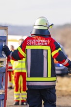 Firefighter from behind in emergency clothing, other emergency personnel in the background, fire