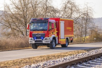 Red fire engine driving along a road with bare trees in the background, fire department exercise on