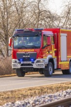 Red fire truck is driving on a country road. Barren winter landscape in the background, fire