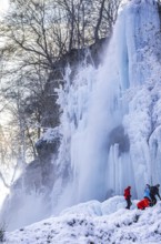 Spectators climb on the Urach waterfall full of bizarre ice formations, frozen at low winter