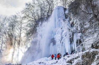 Spectators climb on the Urach waterfall full of bizarre ice formations, frozen at low winter