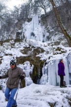 Hikers climb on the Urach waterfall full of bizarre ice formations, frozen at low winter